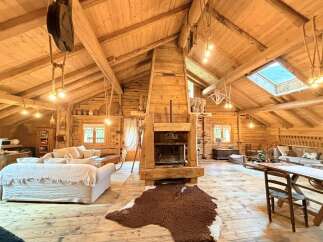 Experience rustic charm in this expansive log cabin living space, featuring a grand wooden fireplace as the centerpiece.