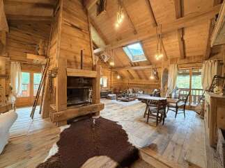 Experience rustic charm in this spacious log cabin living area, featuring a grand stone fireplace and exposed wooden beams throughout.