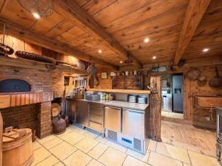 Experience rustic charm in this beautifully appointed kitchen, featuring a traditional brick pizza oven and exposed wooden beams that create a warm, inviting atmosphere.