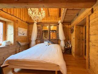 Experience rustic charm in this cozy wooden bedroom, featuring a luxurious crystal chandelier and a plush white duvet.