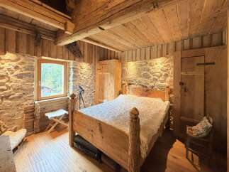 Experience rustic charm in this cozy bedroom, featuring exposed wooden beams and stone walls for an authentic alpine feel.