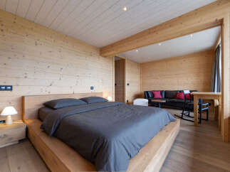 Experience rustic luxury in this charming wooden bedroom, featuring a comfortable bed with dark grey linens and a matching nightstand with a modern lamp.