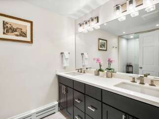 This modern bathroom features a sleek dark wood vanity with a white quartz countertop, complemented by two undermount sinks and stylish brushed nickel faucets.