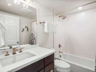 This modern bathroom features a sleek vanity with a white countertop and dark wood cabinets, complemented by stylish bronze fixtures.