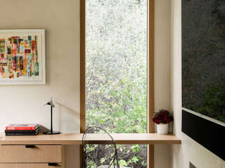 This modern living space features a sleek wooden desk built into a tall window frame, offering a serene view of lush greenery.