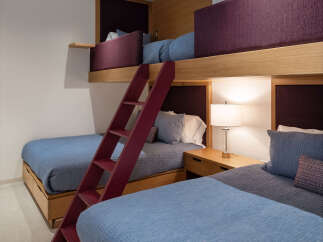 This modern bedroom features a stylish bunk bed setup with plush purple headboards and comfortable blue quilted bedding.