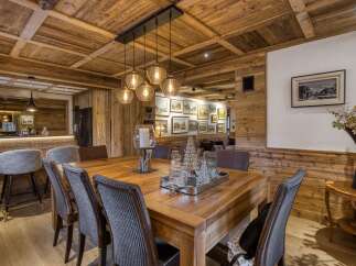 Experience rustic elegance in this mountain lodge dining room, featuring a warm wooden ceiling and walls complemented by a substantial wooden dining table and comfortable seating.