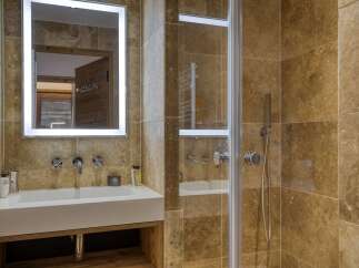 Experience luxury in this modern bathroom featuring a sleek white sink, elegant chrome fixtures, and a spacious walk-in shower with a rainfall showerhead.