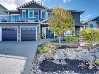 This stunning two-story home boasts a modern dark gray exterior with a three-car garage and a spacious balcony on the upper level.