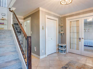 Step into this inviting entryway featuring a plush carpeted staircase with a dark wood banister and ornate metal spindles.