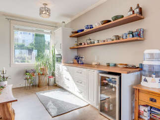 This charming kitchen features a built-in wine fridge and ample storage with white cabinetry and open shelving displaying decorative bowls and mugs.