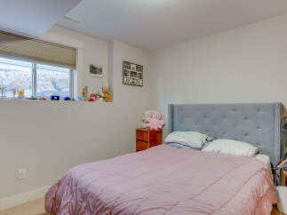 Discover this charming bedroom featuring a comfortable queen-sized bed with a plush pink comforter and a stylish grey tufted headboard.