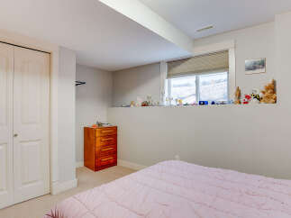 Discover comfort and style in this charming bedroom, featuring a plush pink comforter on a bed, a wooden dresser for storage, and a large window offering natural light.