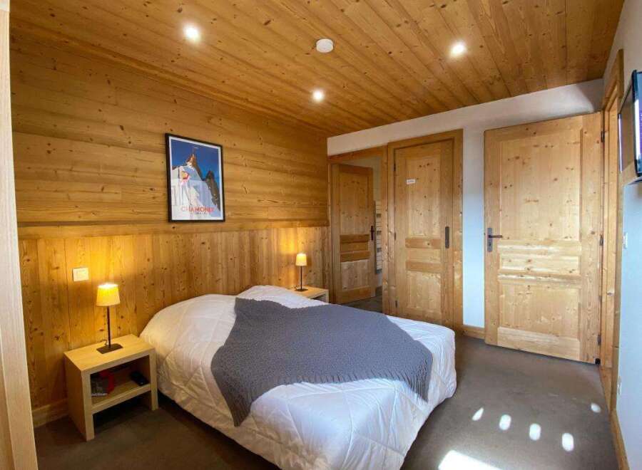 Experience cozy mountain living in this charming bedroom, featuring warm wood paneling and a comfortable bed adorned with a plush grey throw.