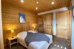 Experience cozy mountain living in this charming bedroom, featuring warm wood paneling and a comfortable bed adorned with a plush grey throw.