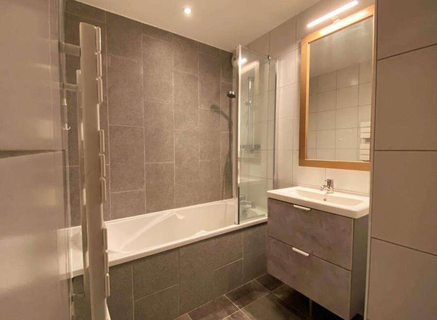 This modern bathroom features a sleek bathtub with a glass shower screen, perfect for relaxing after a long day.