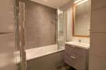 This modern bathroom features a sleek bathtub with a glass shower screen, perfect for relaxing after a long day.