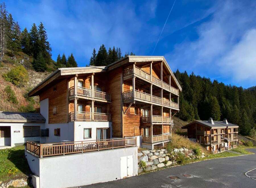 Experience the charm of alpine living in this stunning wooden chalet, nestled against a backdrop of lush green forests and a clear blue sky.