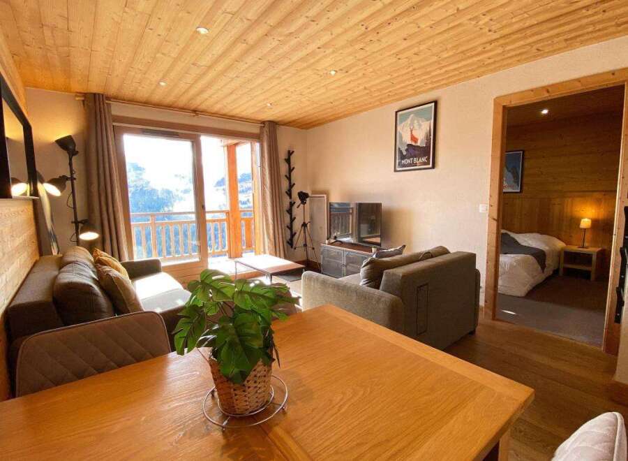 Experience cozy mountain living in this charming apartment, featuring a spacious living area with comfortable seating and a large window offering scenic views.