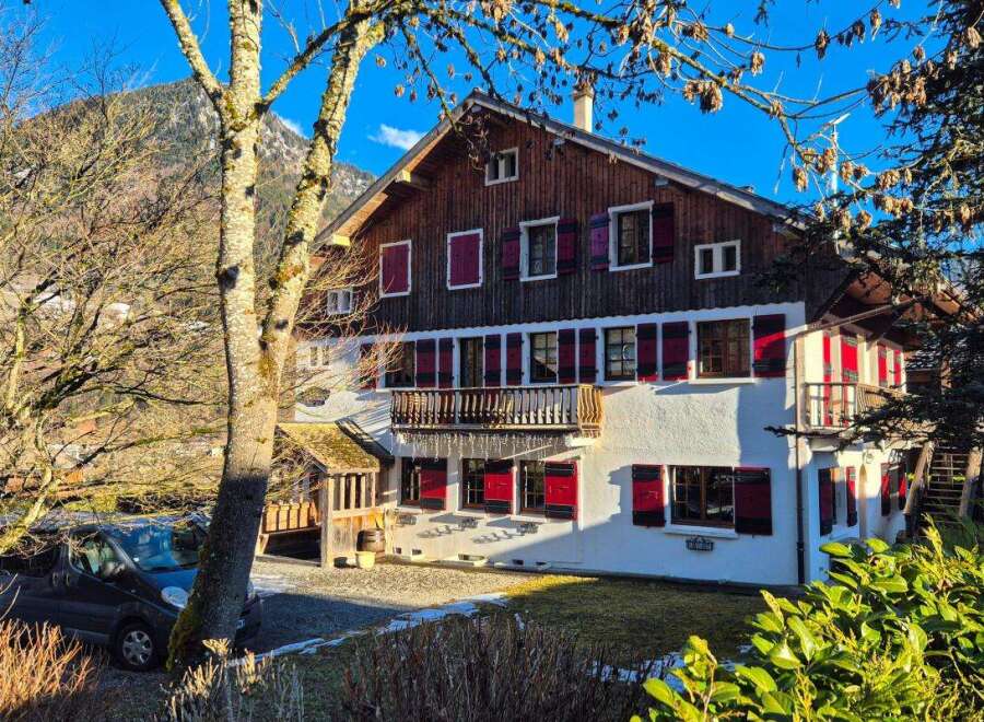 Charming alpine chalet featuring traditional wooden architecture and vibrant red shutters, set against a stunning mountain backdrop.