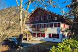 Charming alpine chalet featuring traditional wooden architecture and vibrant red shutters, set against a stunning mountain backdrop.