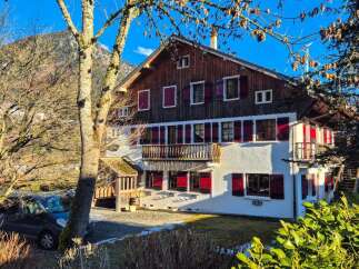 Charming alpine chalet featuring traditional wooden architecture and vibrant red shutters, set against a stunning mountain backdrop.