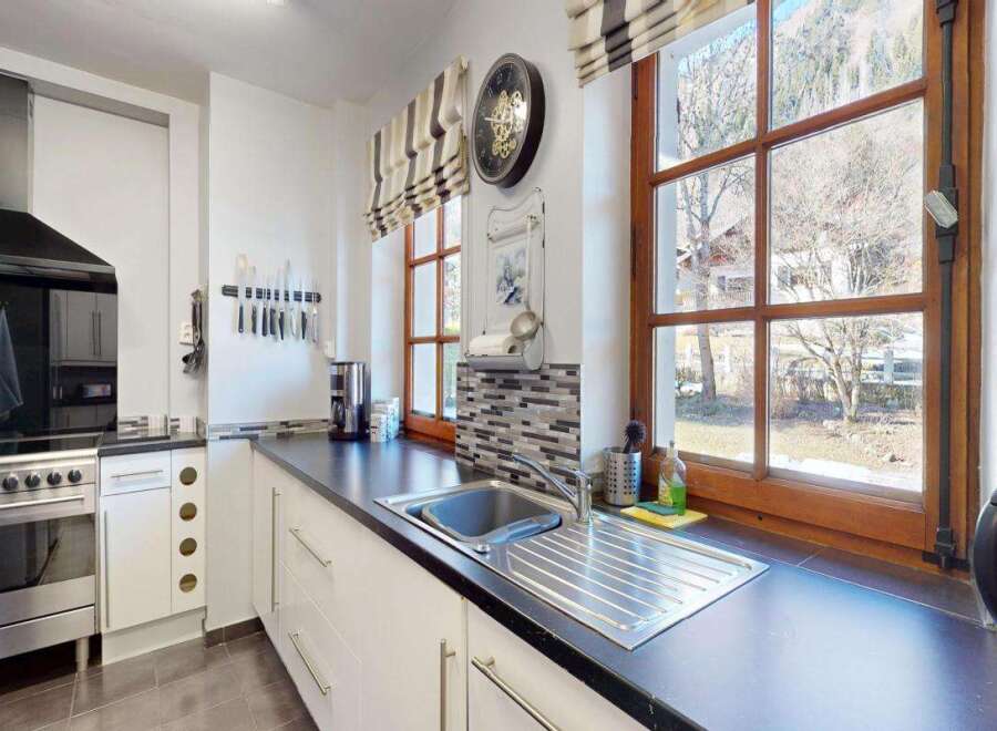 This modern kitchen boasts a sleek stainless steel range with a black glass hood, complemented by a black countertop and white cabinetry.