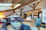 Experience rustic charm in this spacious living area, featuring exposed wooden beams and a vaulted ceiling with skylights for abundant natural light.