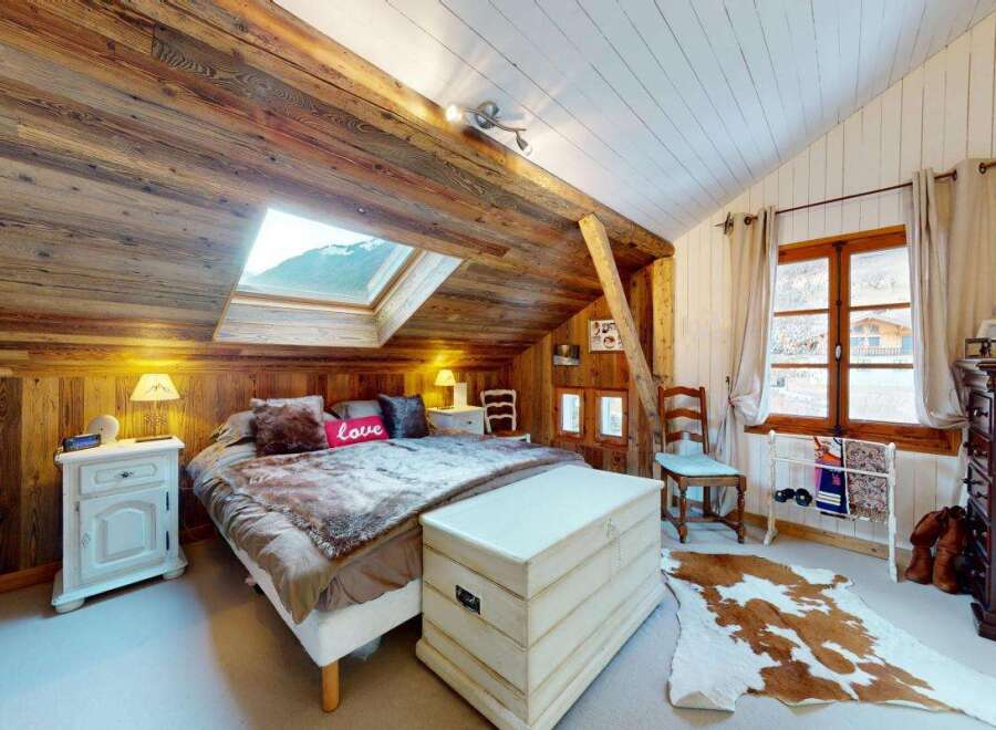 Experience rustic charm in this cozy attic bedroom, featuring exposed wooden beams and a skylight offering mountain views.