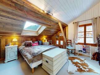 Experience rustic charm in this cozy attic bedroom, featuring exposed wooden beams and a skylight offering mountain views.