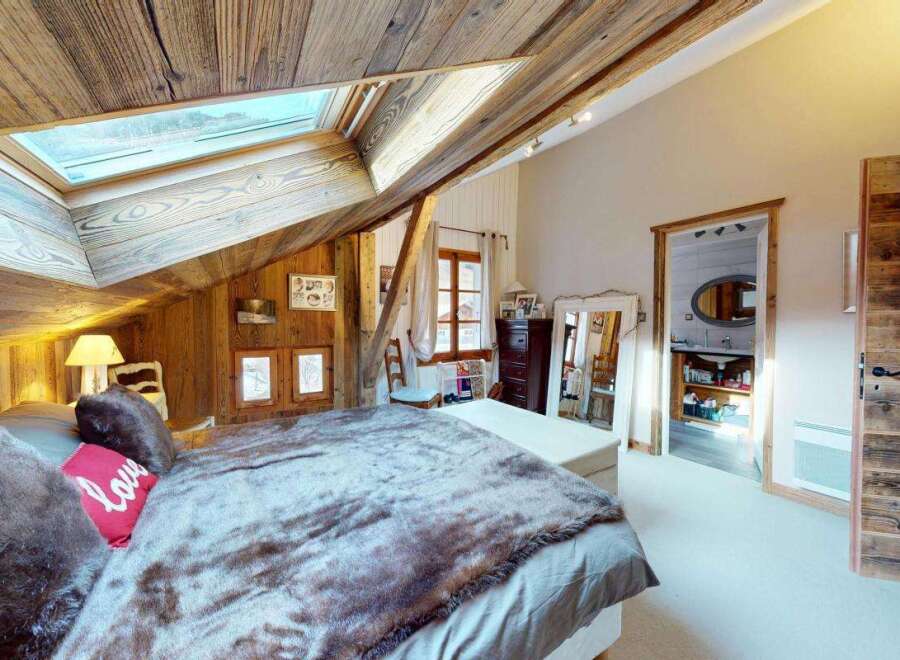 Experience rustic charm in this cozy attic bedroom, featuring a sloped wooden ceiling and a large skylight that floods the space with natural light.