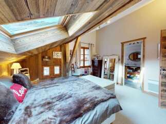 Experience rustic charm in this cozy attic bedroom, featuring a sloped wooden ceiling and a large skylight that floods the space with natural light.
