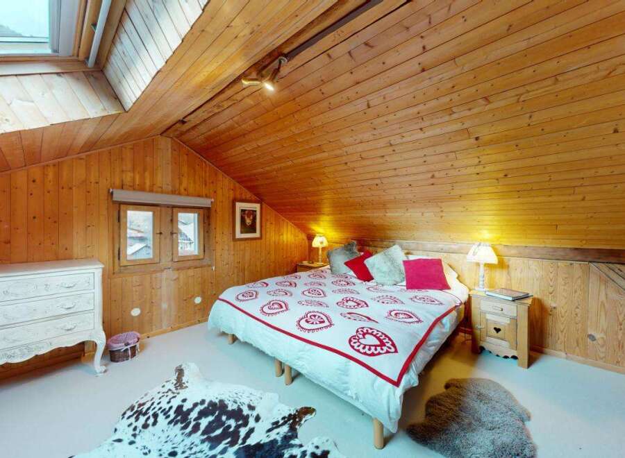 Experience cozy alpine living in this charming attic bedroom, featuring warm wooden paneling and a skylight for natural light.