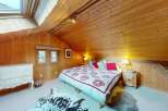 Experience cozy alpine living in this charming attic bedroom, featuring warm wooden paneling and a skylight for natural light.