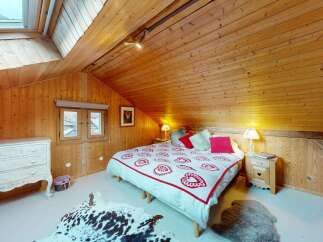 Experience cozy alpine living in this charming attic bedroom, featuring warm wooden paneling and a skylight for natural light.