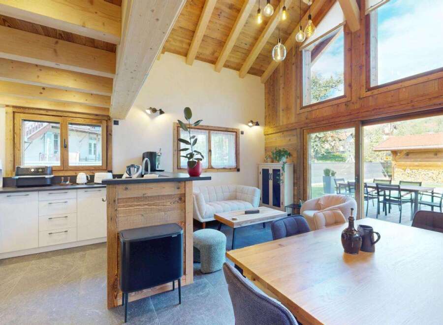 Experience modern alpine living in this stunning open-plan kitchen and dining area, featuring a sleek white kitchen with ample storage and a rustic wooden breakfast bar.