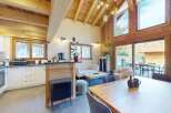 Experience modern alpine living in this stunning open-plan kitchen and dining area, featuring a sleek white kitchen with ample storage and a rustic wooden breakfast bar.