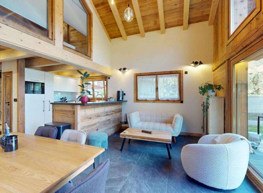 Experience modern alpine living in this stunning open-plan space, featuring a sleek white kitchen with a rustic wooden breakfast bar.