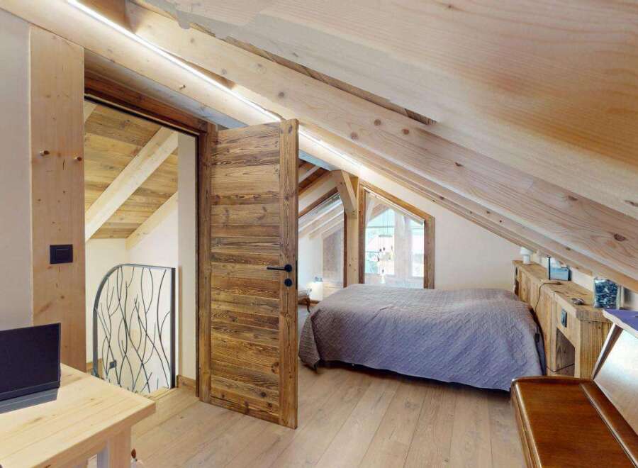 Experience rustic charm in this attic bedroom, featuring exposed wooden beams and a cozy, sloped ceiling.