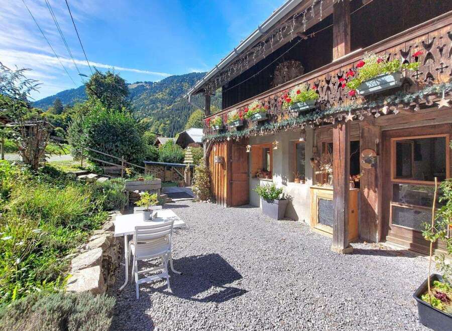 Experience the charm of this rustic mountain retreat, featuring a wooden balcony adorned with vibrant red flowers and intricate carvings.