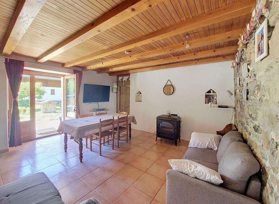 This charming living space features a rustic stone wall and a warm wooden ceiling with exposed beams, creating a cozy and inviting atmosphere.