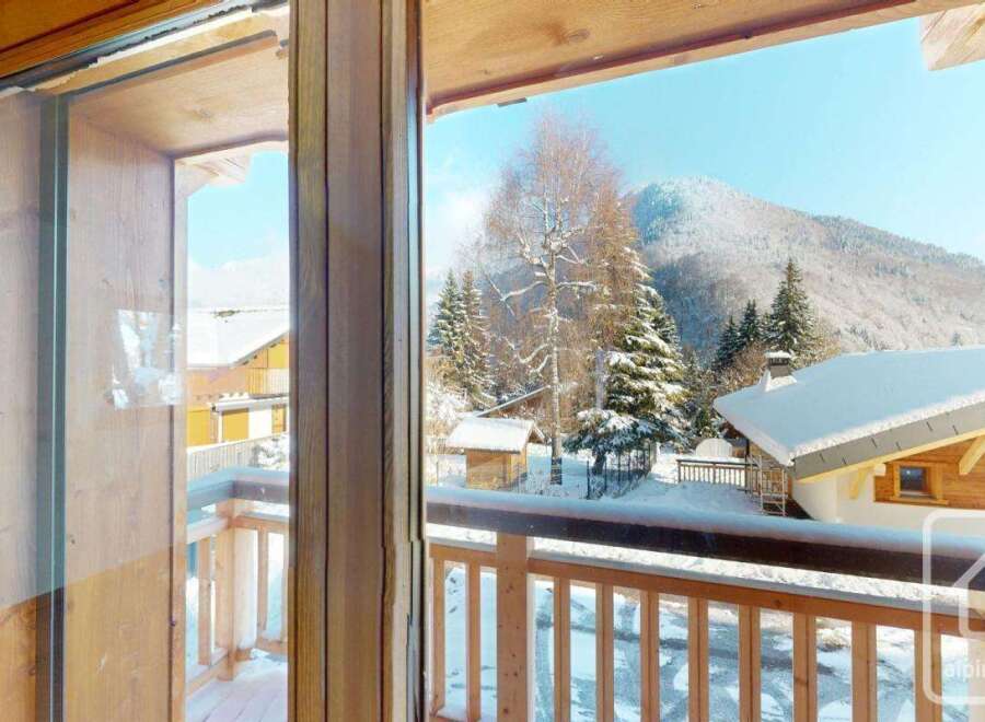 Experience the charm of a winter wonderland from this property's balcony, offering breathtaking views of snow-capped mountains and evergreen trees.