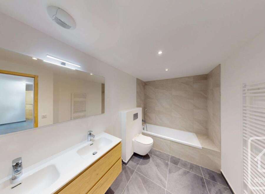 This modern bathroom features a sleek vanity with a double sink, a wall-mounted toilet, and a spacious bathtub.