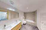 This modern bathroom features a sleek vanity with a double sink, a wall-mounted toilet, and a spacious bathtub.