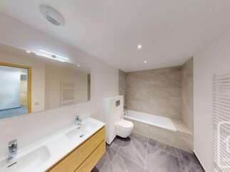 This modern bathroom features a sleek vanity with a double sink, a wall-mounted toilet, and a spacious bathtub.