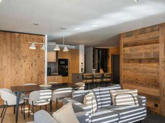 Experience modern alpine living in this beautifully appointed open-concept space, featuring a sleek dining area with a dark wood table and upholstered chairs, adjacent to a contemporary kitchen with wood cabinetry and stainless steel appliances.