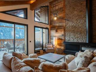 Experience luxury mountain living in this stunning chalet living room, featuring a grand stone fireplace and expansive windows offering breathtaking alpine views.
