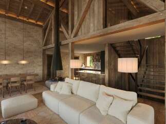 Experience rustic luxury in this stunning open-concept living space, featuring a soaring vaulted ceiling with exposed wooden beams and a dramatic floor-to-ceiling fireplace.