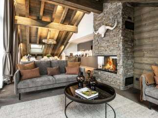 Experience ultimate luxury in this stunning mountain chalet, featuring a grand stone fireplace and exposed wooden beams that create a warm, inviting atmosphere.