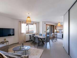 This modern open-plan living space features a comfortable sofa area with a large TV, a stylish dining table with six chairs, and a fully equipped kitchen.